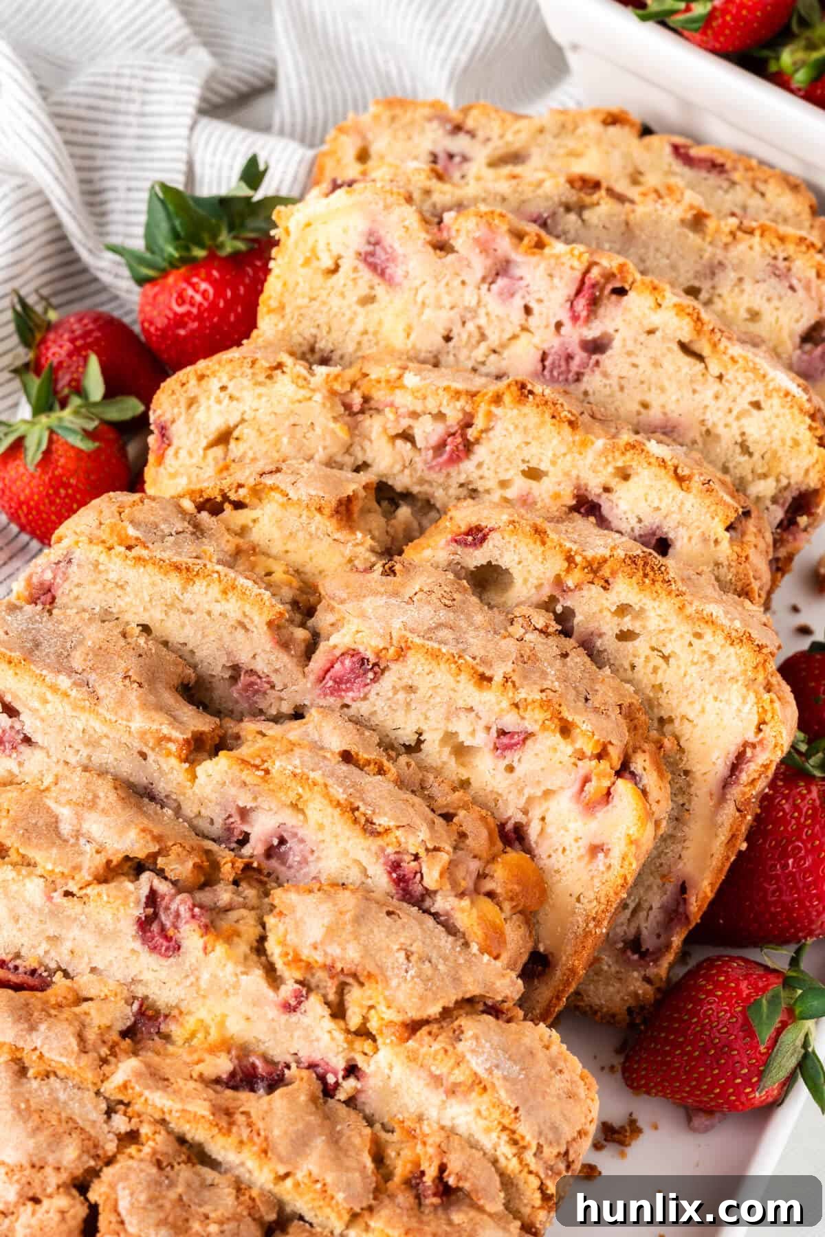 Strawberry Cheesecake Bread 15 Sliced strawberry bread with cream cheese swirls arranged on a white platter, garnished with whole strawberries.