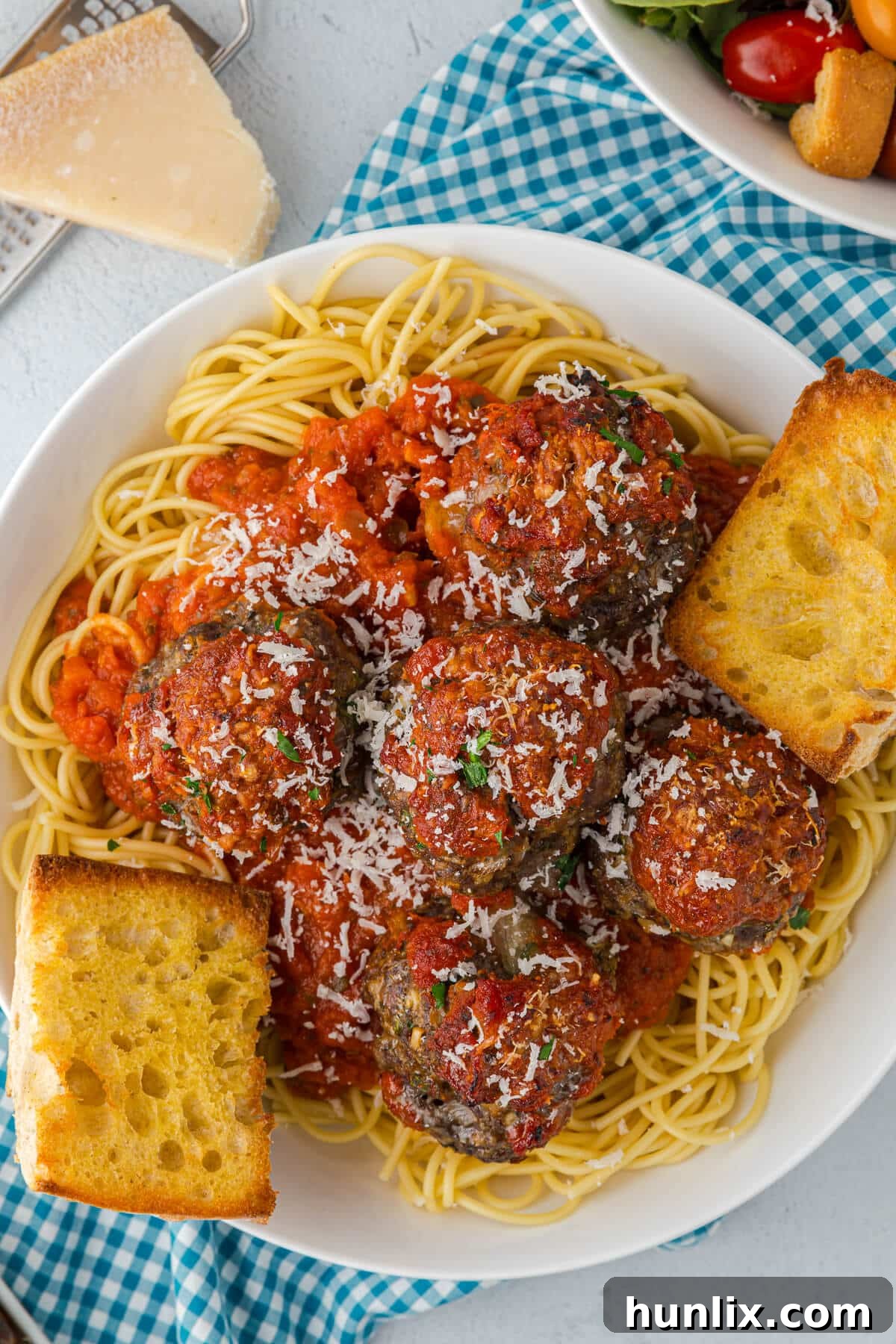 A plate of spaghetti with cheesy meatballs and garlic bread, highlighting the melted cheese inside.