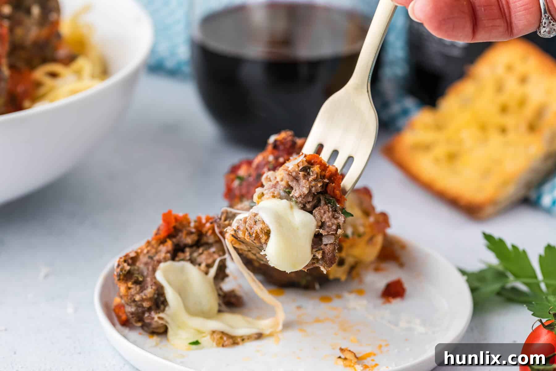 A single cheesy meatball perfectly impaled on a fork, showing its delightful texture.