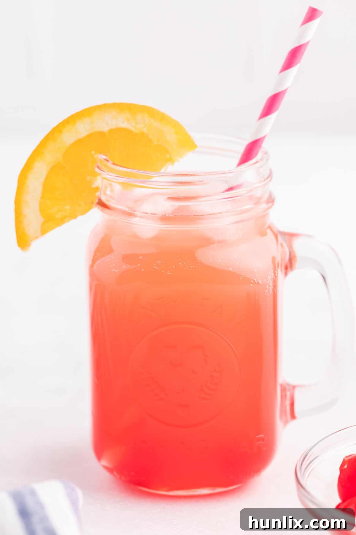 A Shirley Temple drink in a glass mug with a straw and an orange slice for garnish.