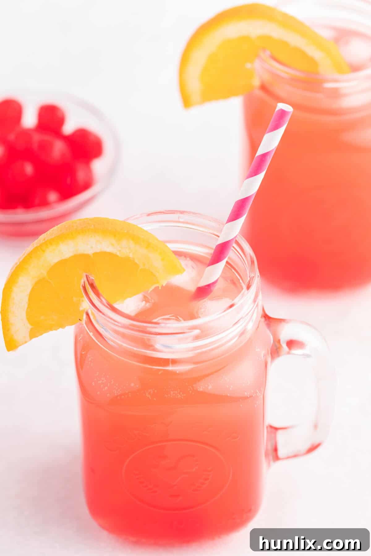 The finished Shirley Temple recipe in a glass with a straw and an orange slice for garnish, seen from eye level.