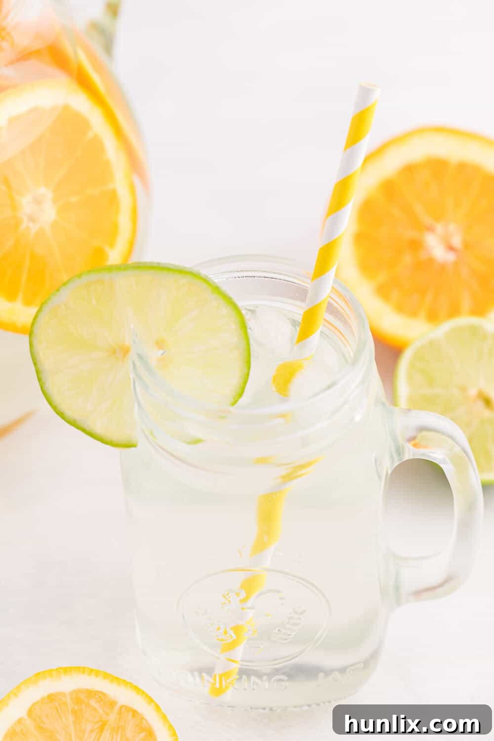 A refreshing glass mug of Citrus Bliss Infused Water, complete with a straw and a vibrant slice of lime on the rim, showcasing the perfect serving.