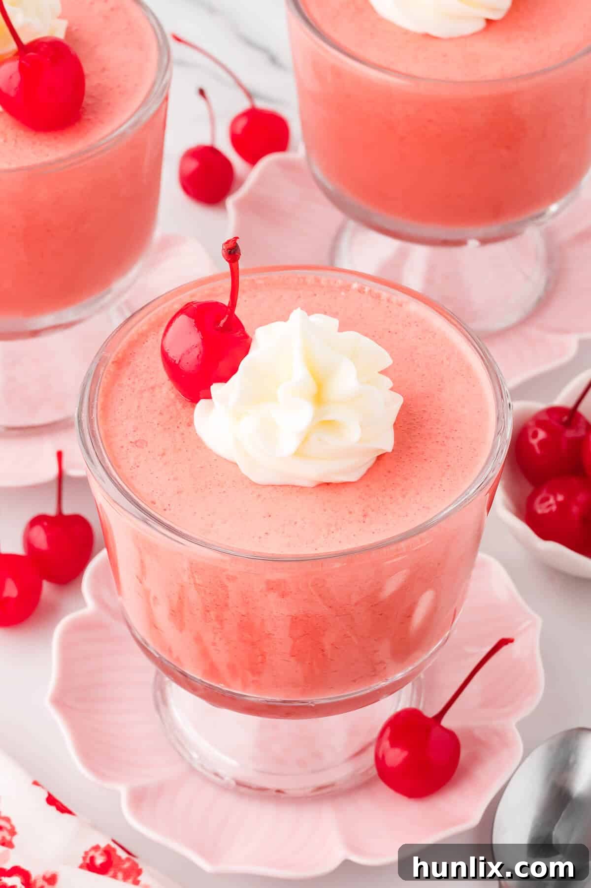 Velvet Cherry Dream 2 Individual parfait dishes filled with light pink cherry mousse, garnished with fresh cherries and whipped cream, ready to serve.