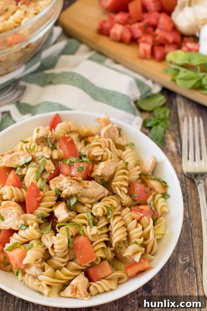 A serving spoon lifting a portion of Bruschetta Chicken Pasta Salad from a large bowl.