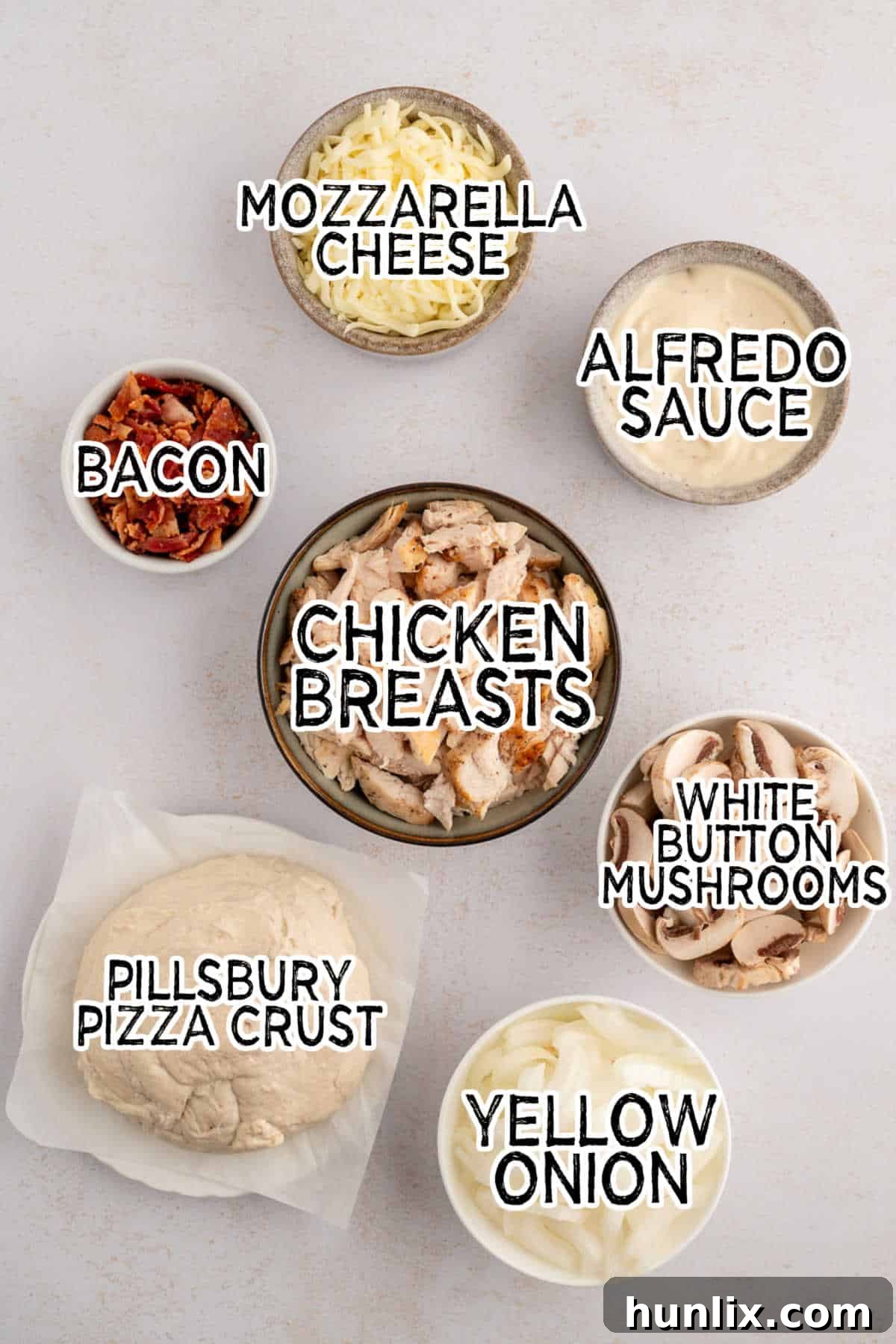 A vibrant display of fresh ingredients laid out, including sliced mushrooms, diced onions, cooked chicken, crispy bacon, and a jar of Alfredo sauce, all ready to assemble a delicious chicken bacon alfredo pizza.