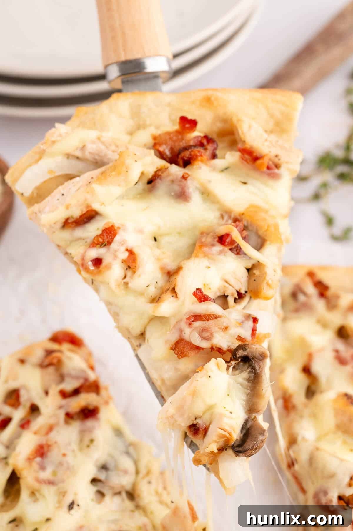 A single slice of Chicken Bacon Alfredo Pizza artfully placed on a spatula, ready to be served, highlighting the golden crust, creamy sauce, and generous toppings.
