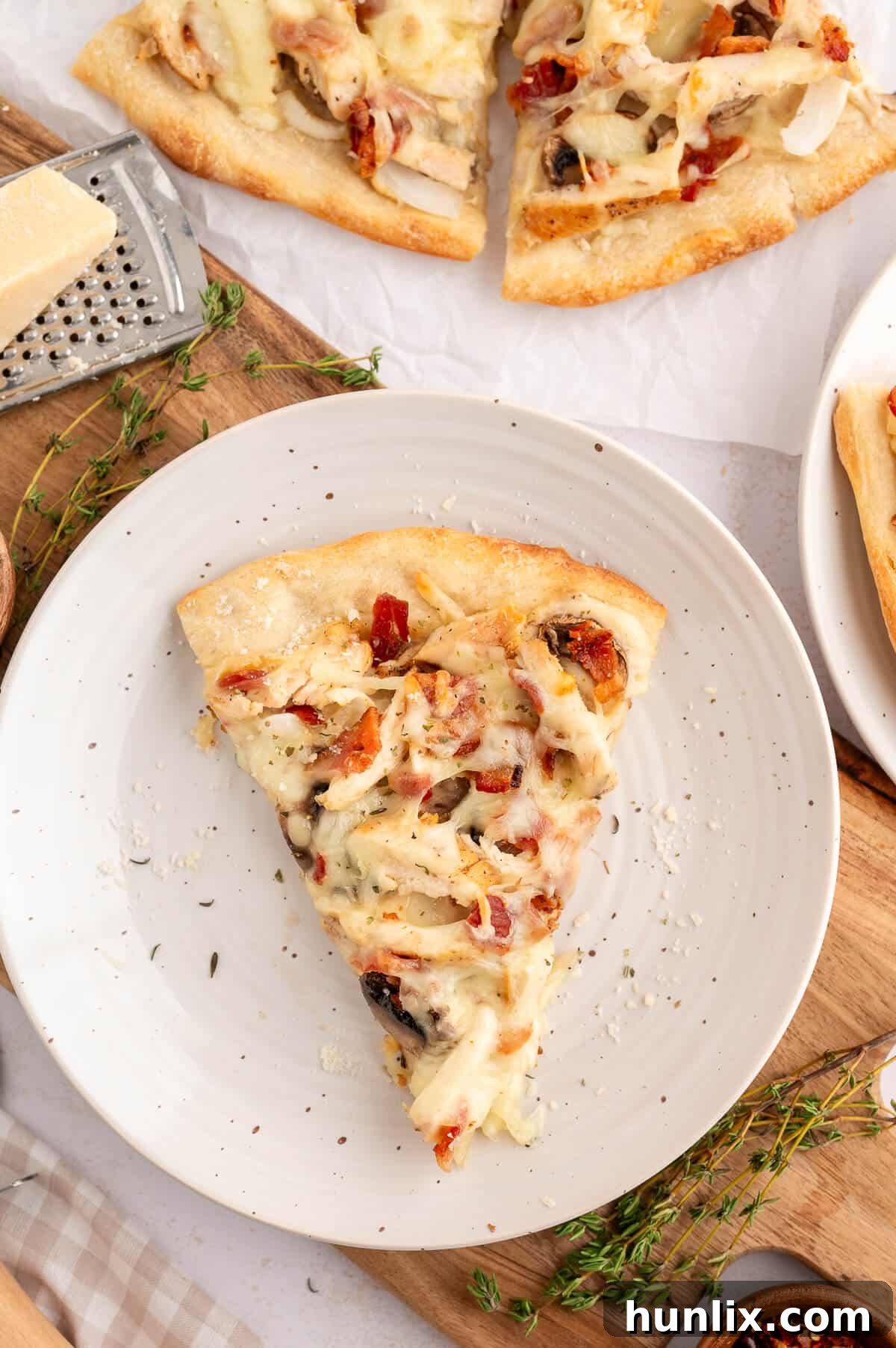 A generous slice of Chicken Bacon Alfredo Pizza resting on a white plate, highlighting its creamy white sauce, tender chicken, crispy bacon, and melted mozzarella cheese on a golden crust.
