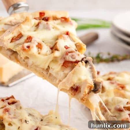Close-up shot of a single slice of Chicken Bacon Alfredo Pizza on a spatula, showcasing the delicious blend of creamy white sauce, chicken, bacon, and melted cheese, with a golden-brown crust.