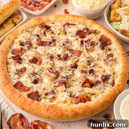 A whole Chicken Caesar Pizza surrounded by fresh ingredients like lettuce, cherry tomatoes, and Parmesan cheese.