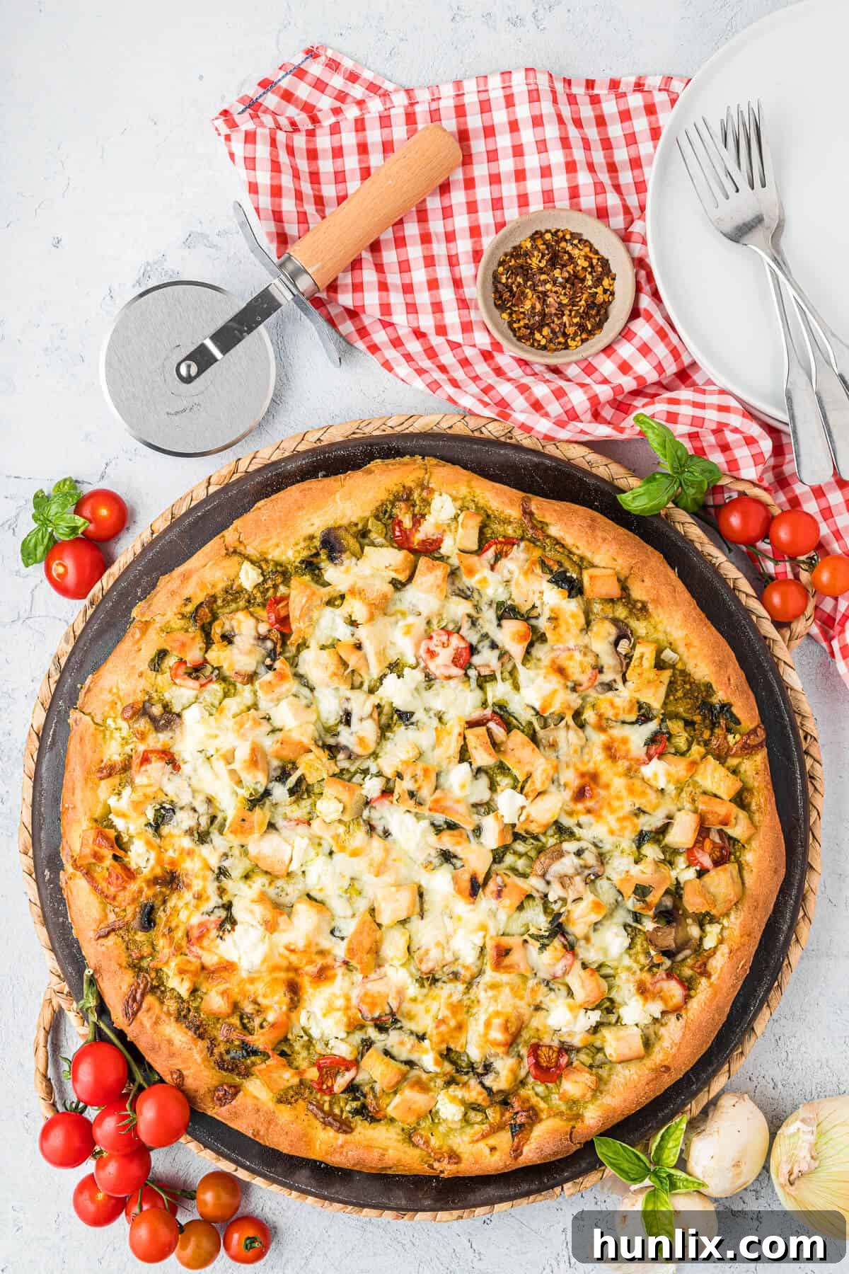 A chicken pesto pizza on a pizza pan, freshly baked with golden crust and melted cheese.