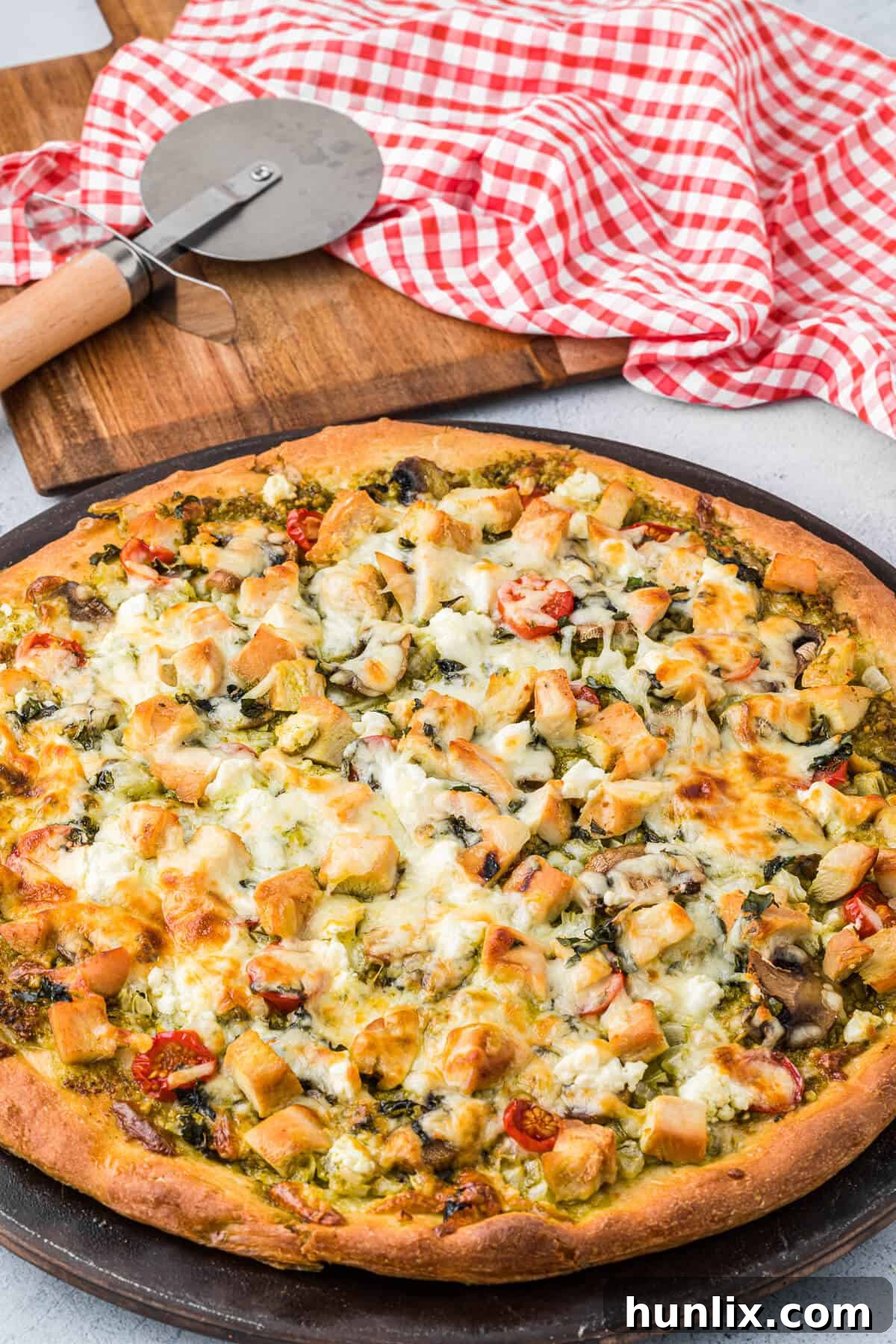 A whole chicken pesto pizza on a metal pizza pan, ready to be sliced and served.