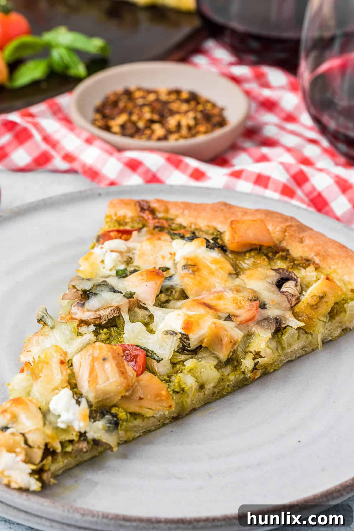 A perfectly cut slice of chicken pesto pizza resting on a white plate, showcasing the crispy crust and melted toppings.