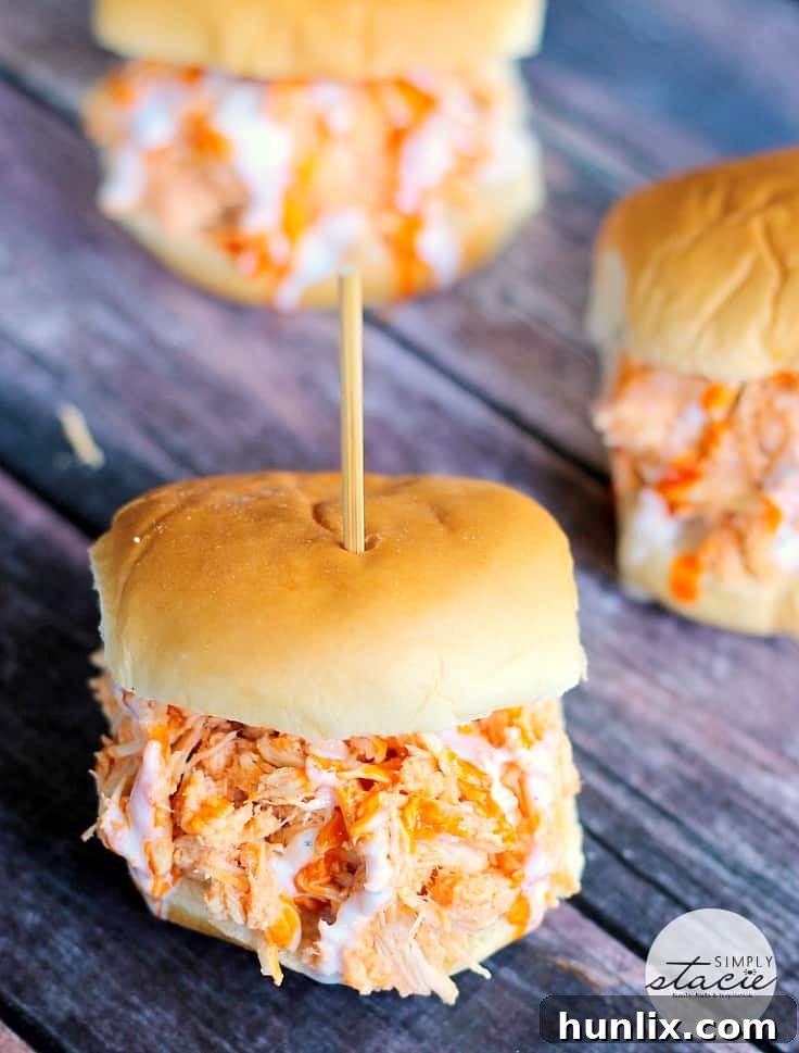 Four delicious Slow Cooker Buffalo Chicken Sliders on a serving board with ranch and celery sticks.