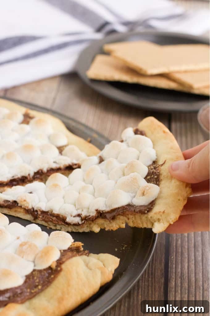 Gooey Smores Dessert Pizza 4 Freshly baked S'mores Pizza being removed from the oven, with perfectly toasted marshmallows and melted chocolate, ready to be served.