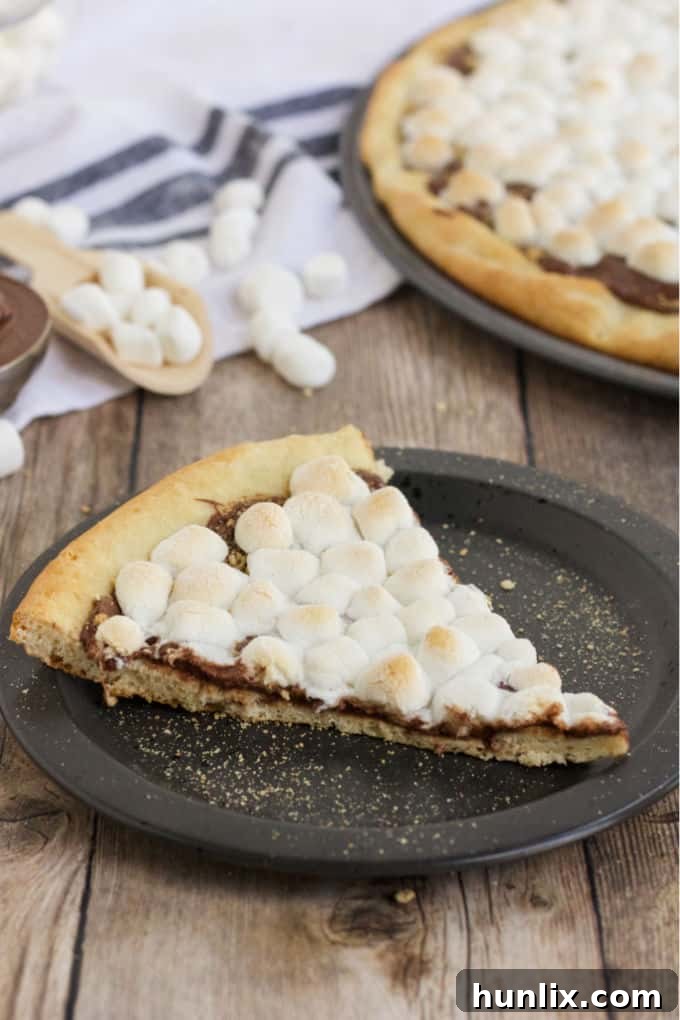 Gooey Smores Dessert Pizza 5 A delicious slice of S'mores Pizza on a plate, showcasing the melted chocolate, toasted marshmallows, and graham cracker crust, ready to be enjoyed.