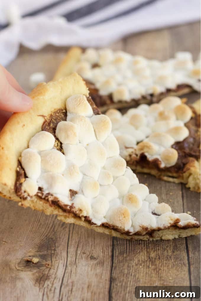 Gooey Smores Dessert Pizza 8 A full, uncut S'mores Pizza on a wooden cutting board, surrounded by fresh ingredients like marshmallows and graham crackers.