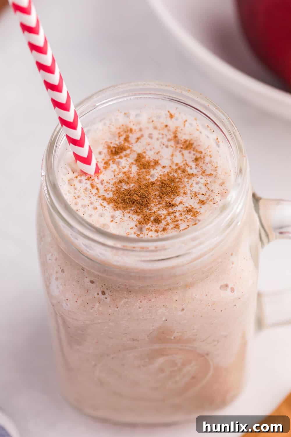 Autumn Spiced Apple Blend 3 The Apple Spice Smoothie recipe in a glass on a white surface with a red and white striped straw, showing its thick texture.