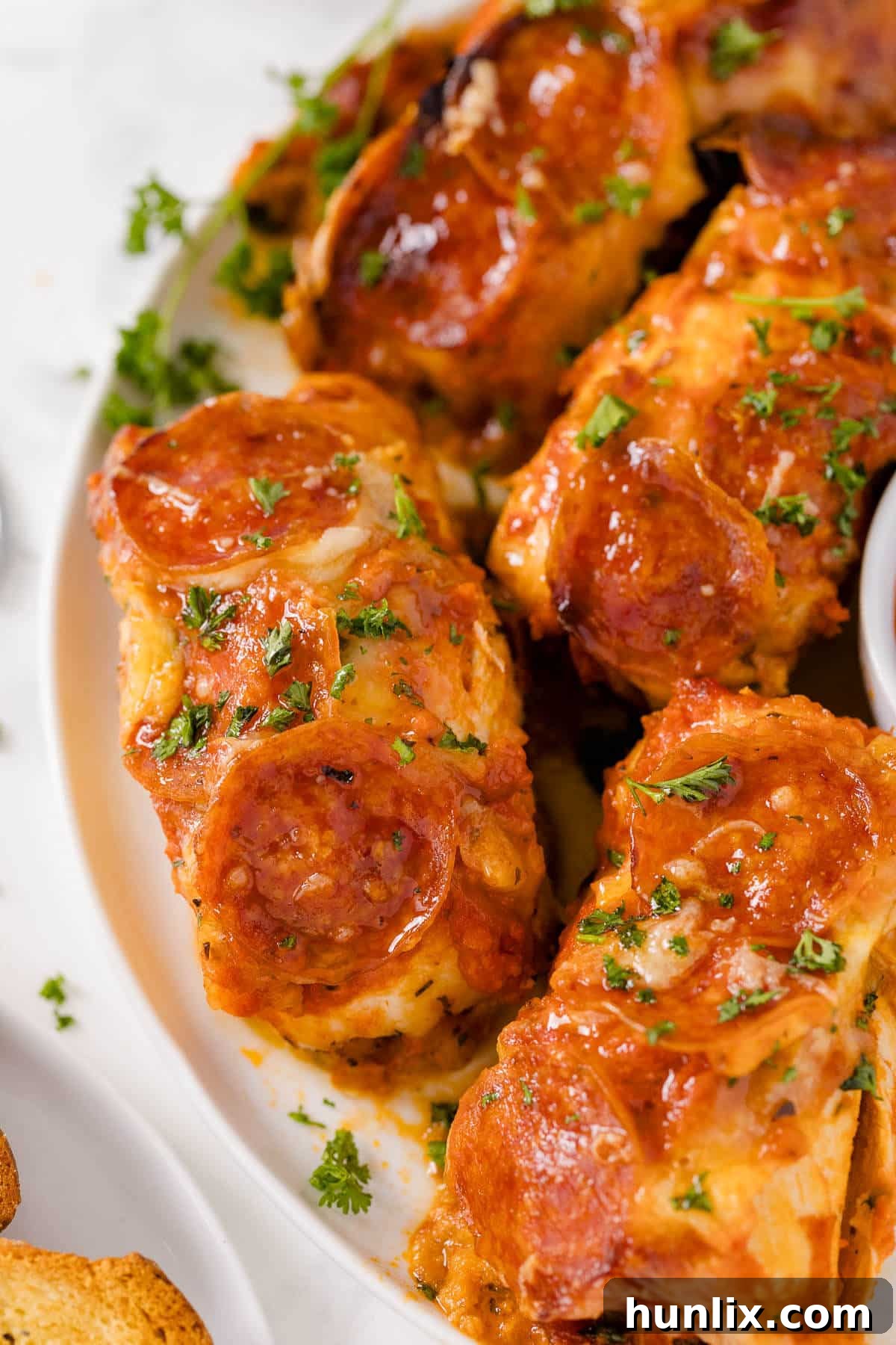 A plate featuring a perfectly baked pizza stuffed chicken, garnished with fresh herbs.