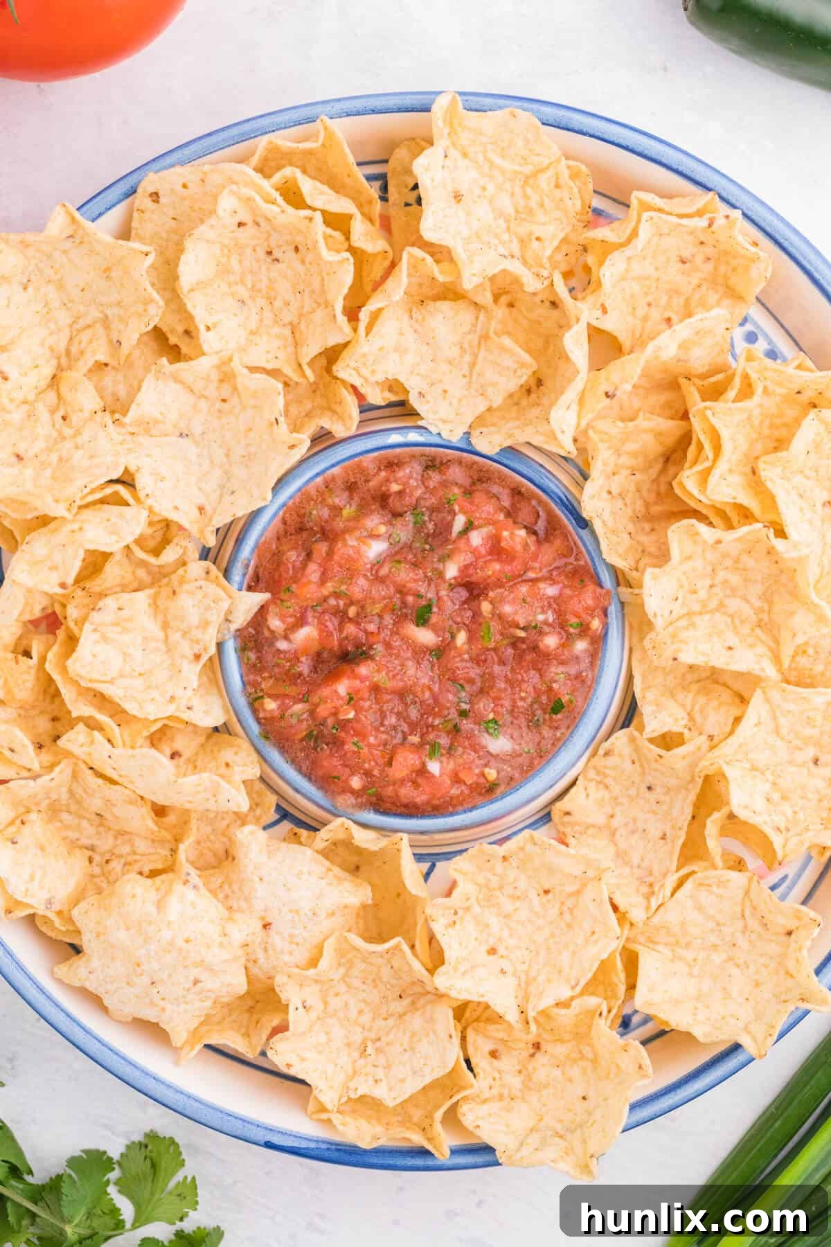 A generous bowl of homemade garden salsa presented on a wooden serving tray, surrounded by a pile of crisp tortilla chips, ready for a feast.
