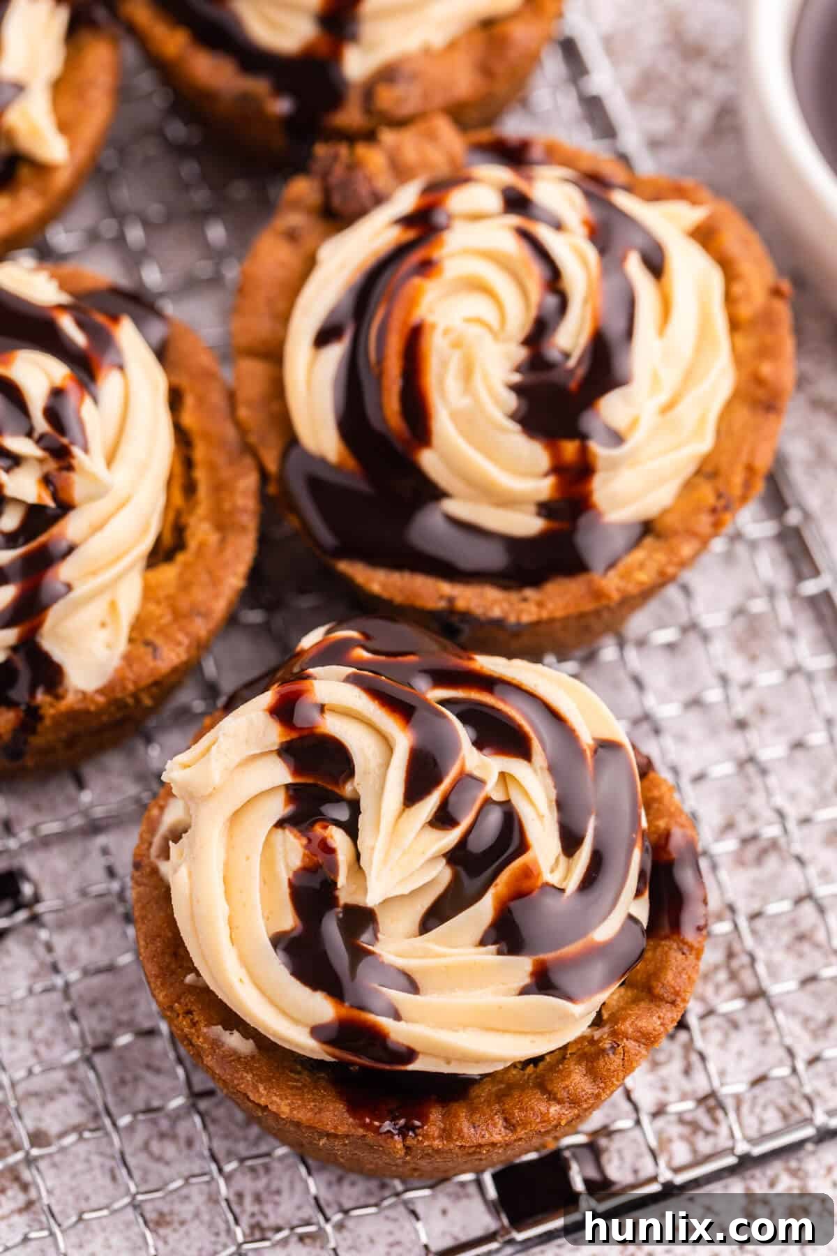 Delicious Reese's Peanut Butter Cookie Cups 4 A trio of freshly baked Reese's cookie cups, drizzled with chocolate sauce, cooling on a wire rack.