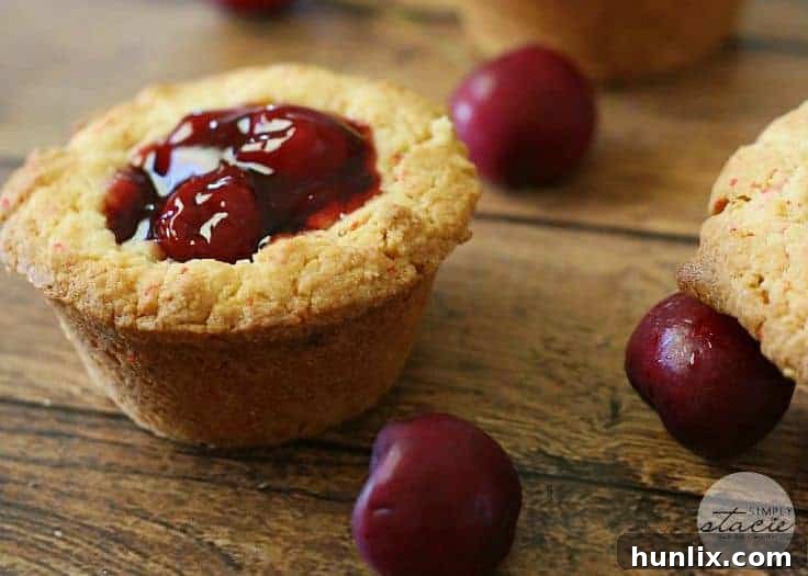Two glistening Cherry Cake Cups nestled in a muffin tin, showcasing their perfect cup shape and glossy cherry filling before serving.
