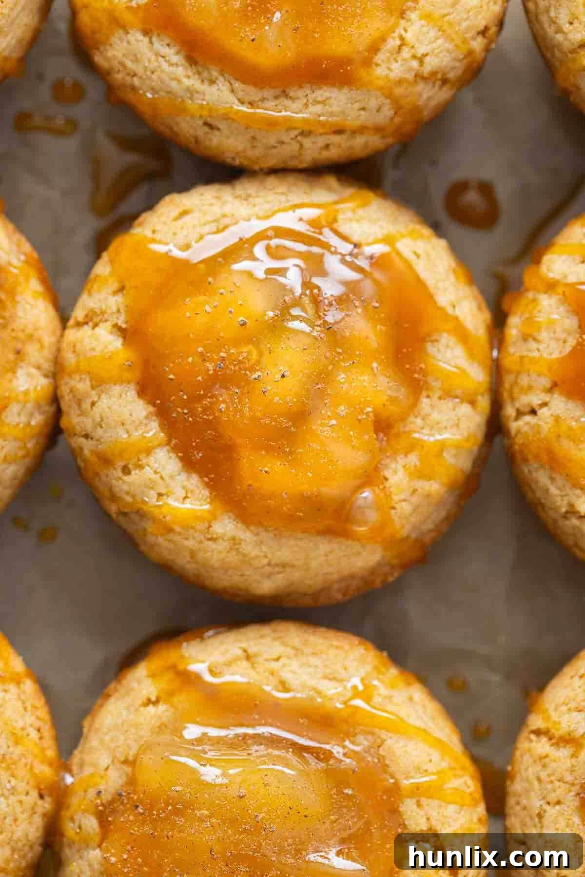 Caramel apple cake cups on a baking sheet, golden-brown and glistening with caramel.