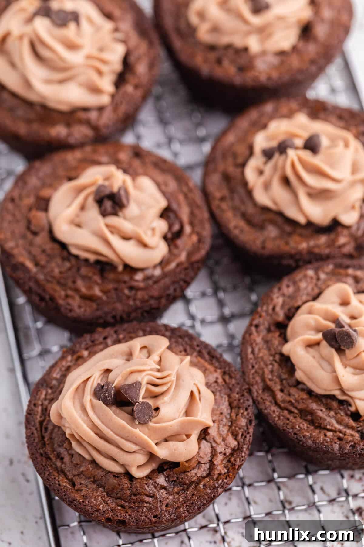 Decadent Brownie Cheesecake Bites 2 Delightful Brownie Cheesecake Cups arranged neatly on a wire cooling rack, showcasing their perfect shape and inviting chocolate topping.