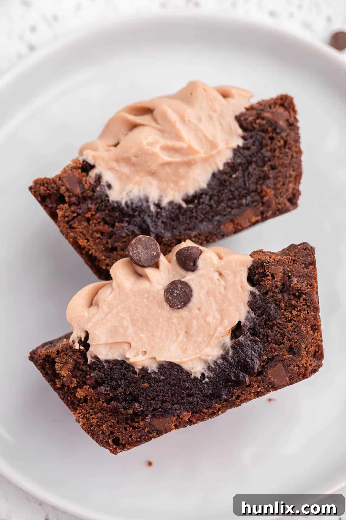 Decadent Brownie Cheesecake Bites 6 A brownie cheesecake cup is elegantly cut in half on a white plate, revealing its distinct layers of fudgy brownie and creamy cheesecake filling.