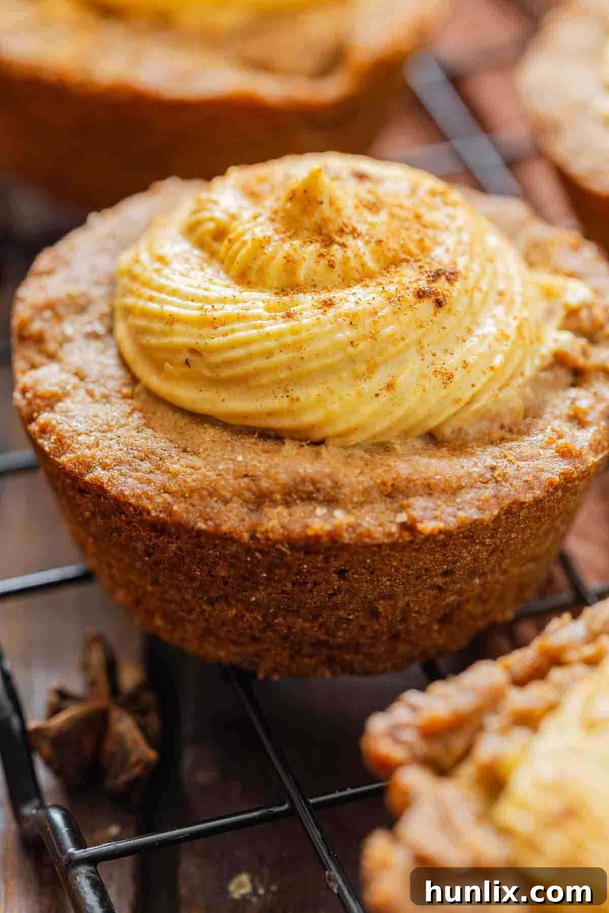 Autumn's Embrace Cakelets 2 A perfectly baked pumpkin spice cake cup, beautifully topped with creamy pumpkin cheesecake filling, resting on a wire rack, ready to be enjoyed.