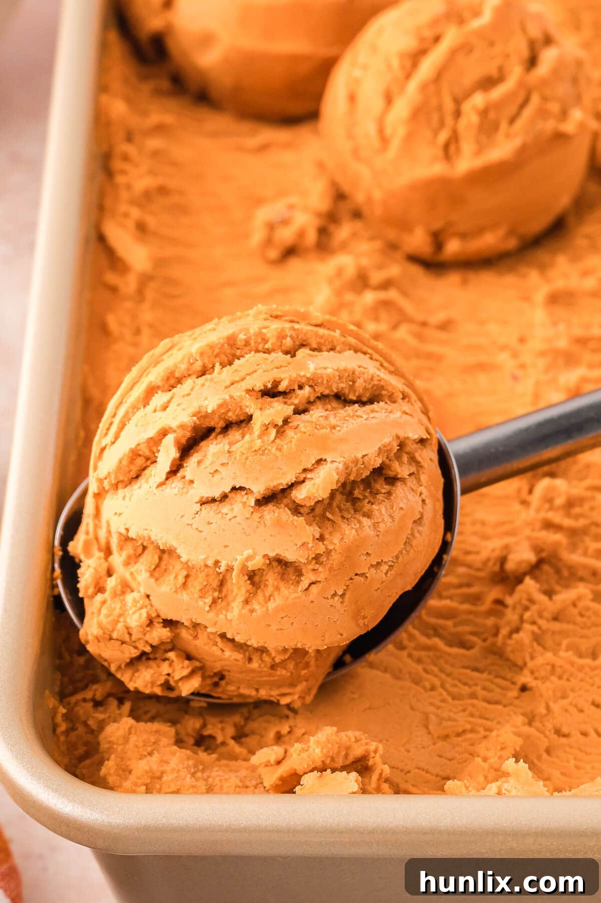 The finished pumpkin pie ice cream in a container with an ice cream scoop resting on the side.