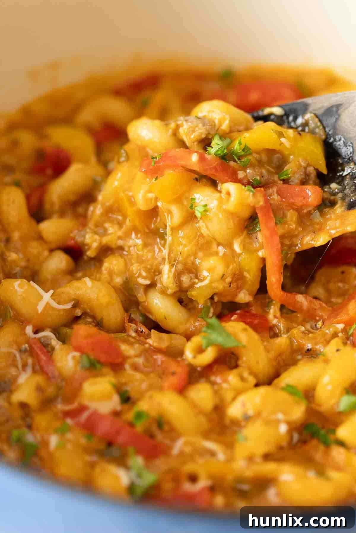 Spicy Sausage Skillet Pasta with Peppers 7 A serving spoon lifting spicy sausage and pepper pasta from a pot, showcasing its rich texture and ingredients.