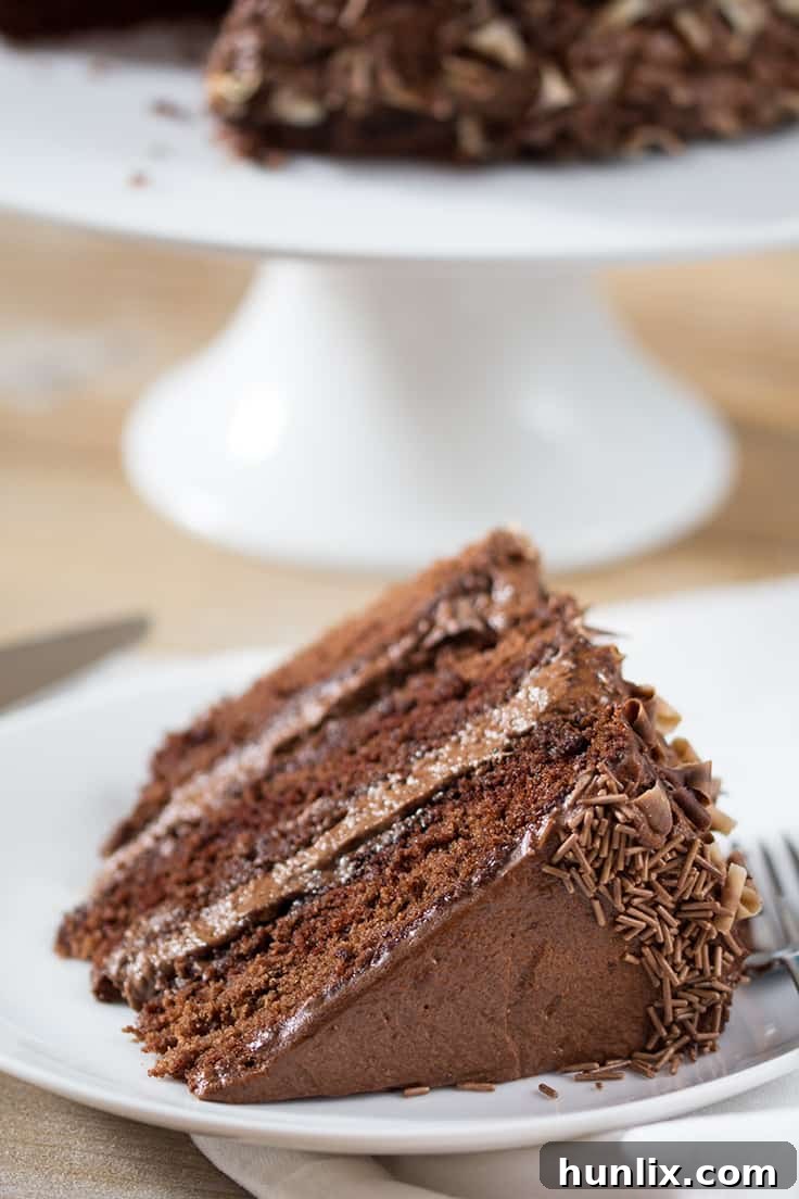 The perfect slice of Chocoholics Chocolate Mousse Cake, showcasing its triple layers, rich mousse, and elegant chocolate curls. A truly irresistible homemade dessert.
