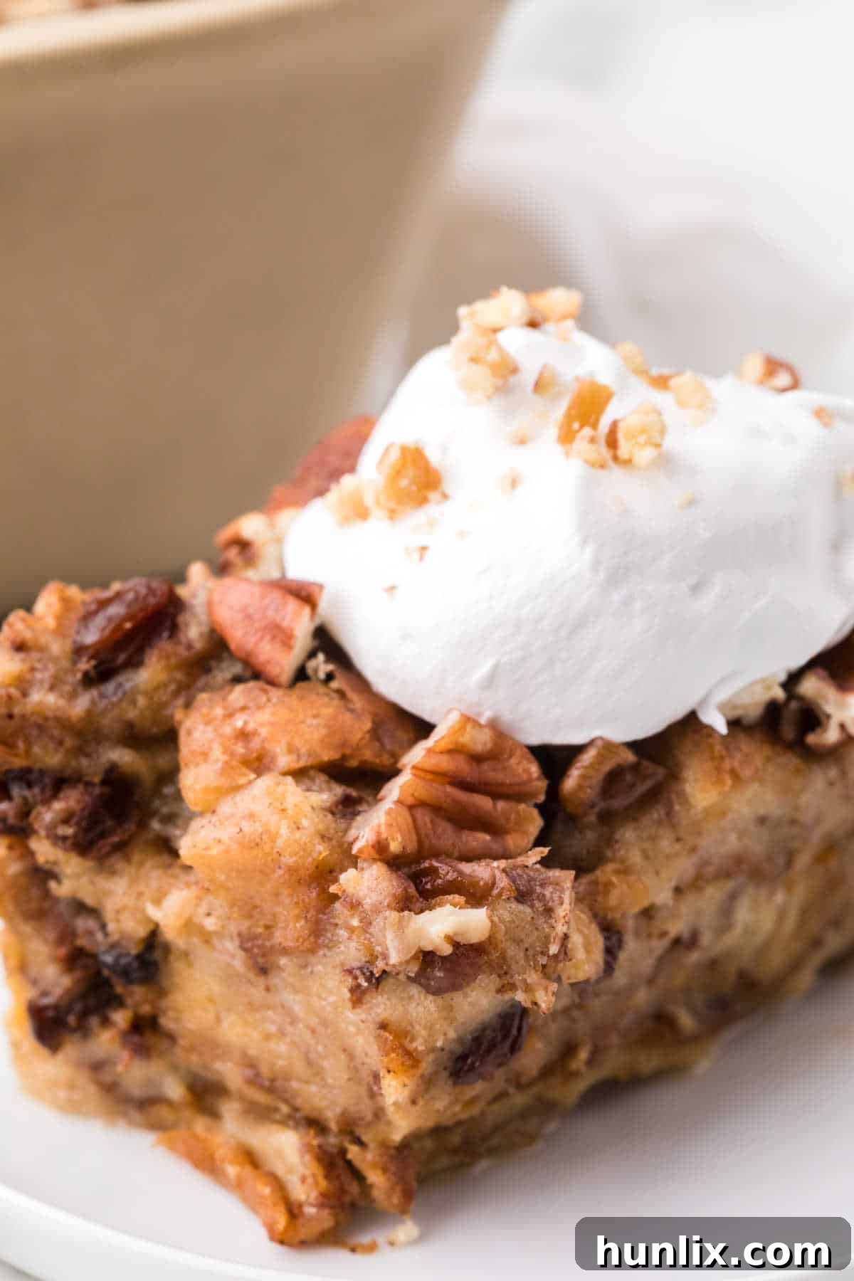 A perfectly golden slice of Slow Cooker Cinnamon Raisin Bread Pudding, topped with a dollop of fluffy whipped cream, resting on a white plate. The pudding is moist and rich with visible raisins and cinnamon swirls.
