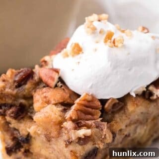 A slice of cinnamon raisin bread pudding on a plate topped with whipped cream.