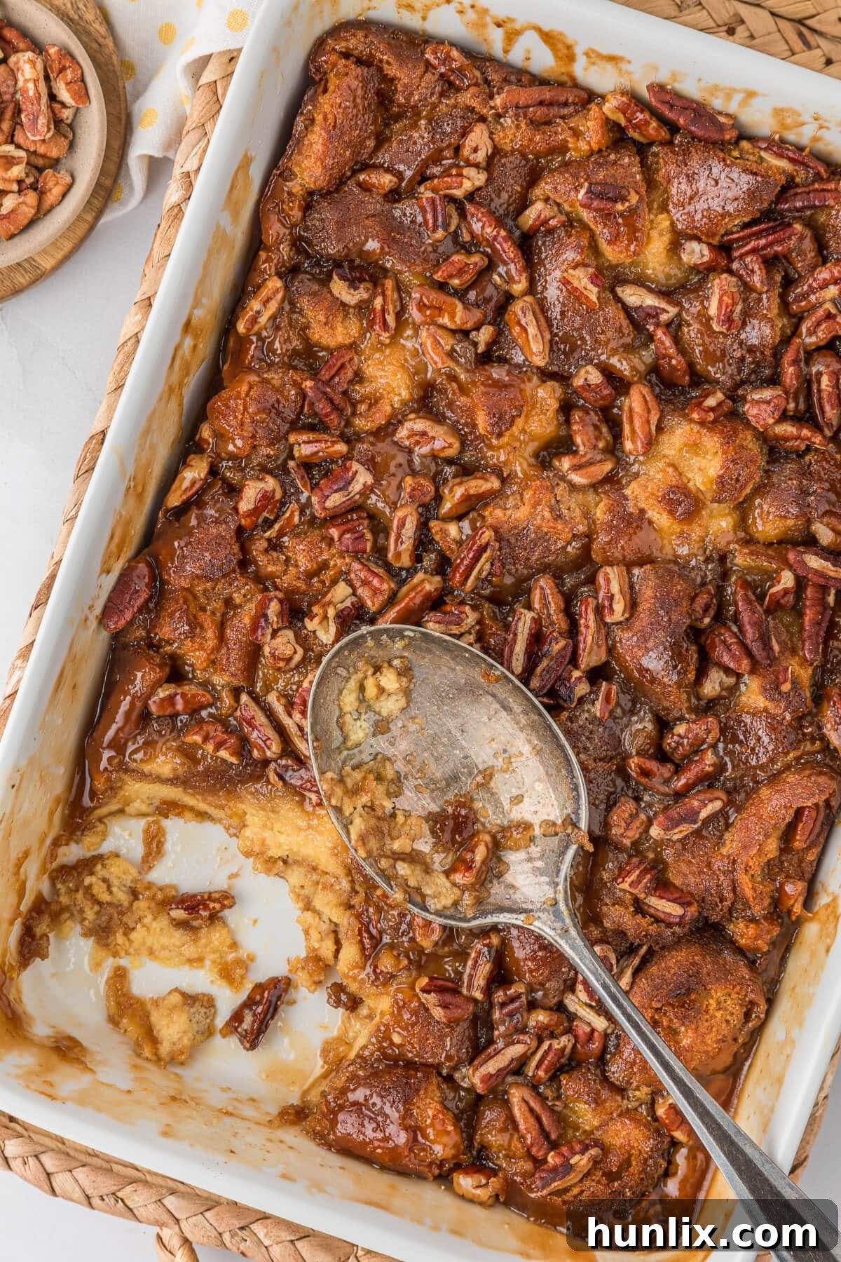 A glorious Caramel Pecan Breakfast Casserole, perfectly baked in a white pan, with a serving spoon poised for a decadent scoop.