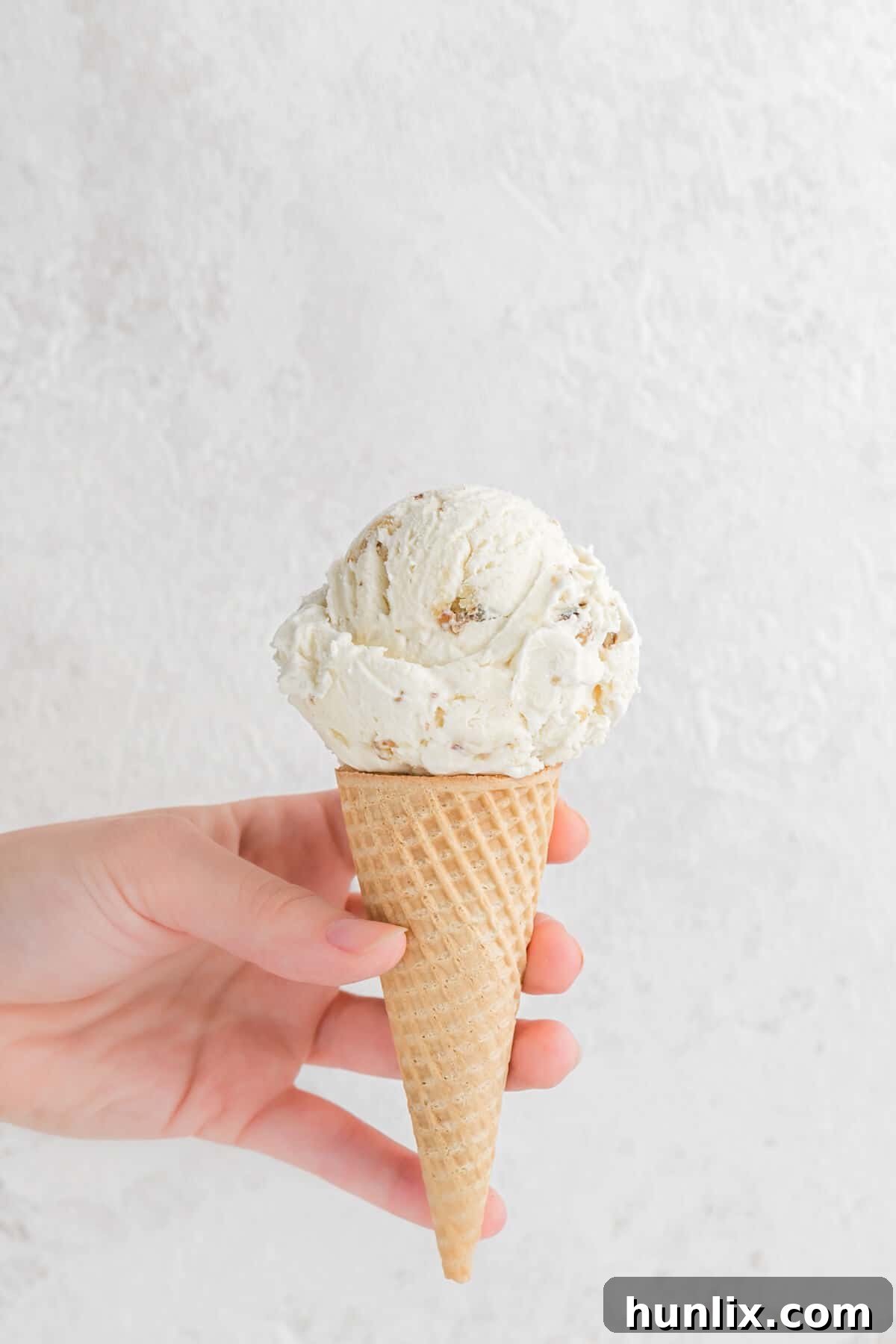 A hand holding a maple walnut ice cream cone.