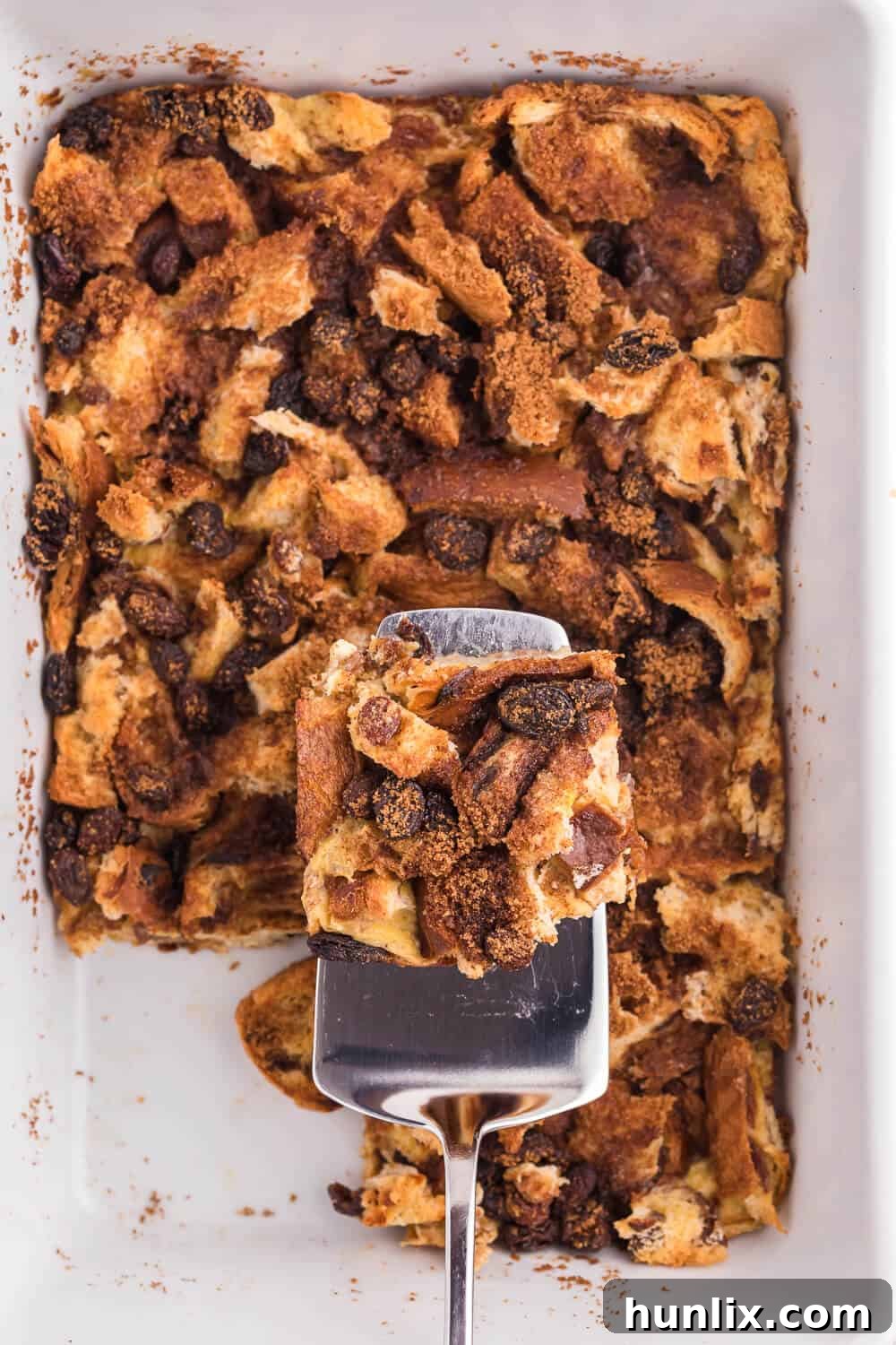 A single slice of Cinnamon Raisin Breakfast Casserole being lifted from the pan with a serving spatula, showcasing its custardy interior.