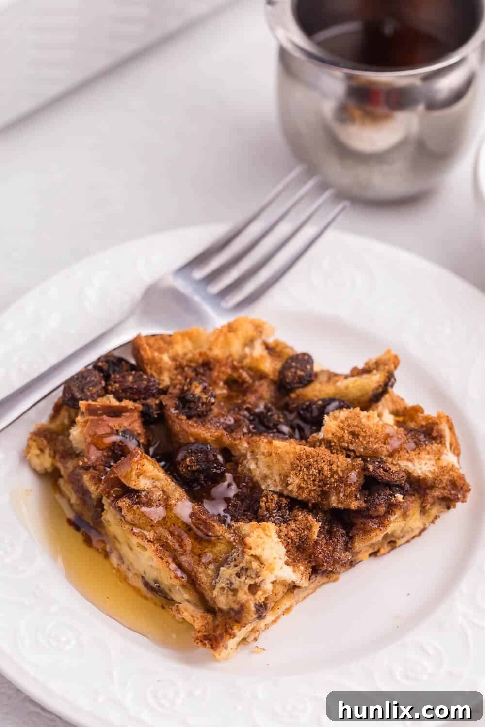 A slice of Cinnamon Raisin Breakfast Casserole on a plate with a fork, ready to be enjoyed, showing its soft texture.