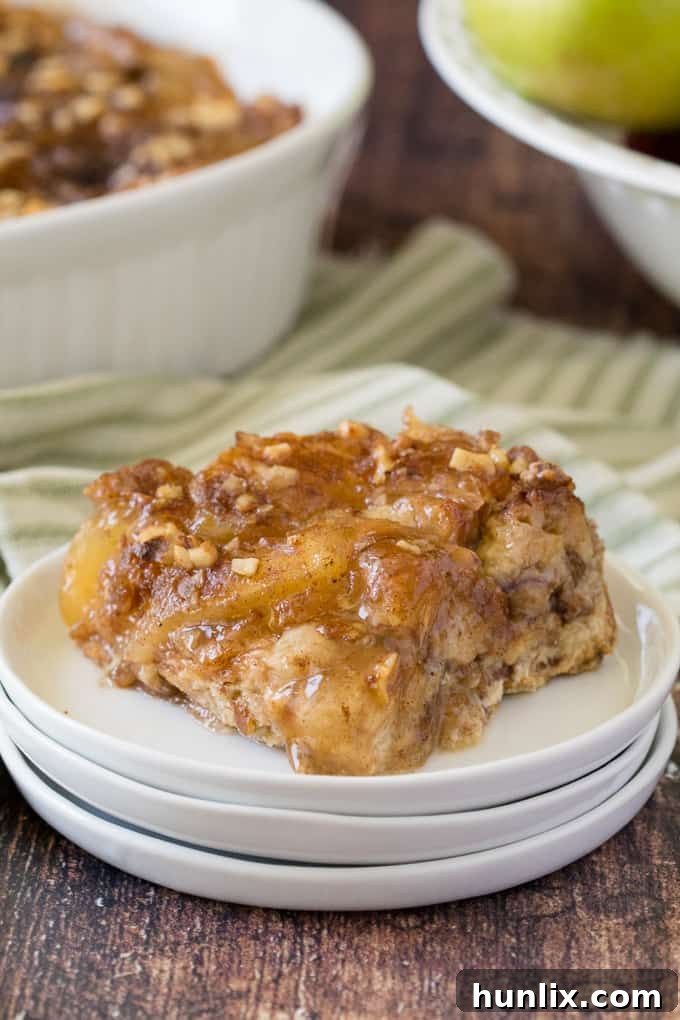 A single slice of Apple Pie French Toast Casserole served on a white plate, with more casserole visible in the background.
