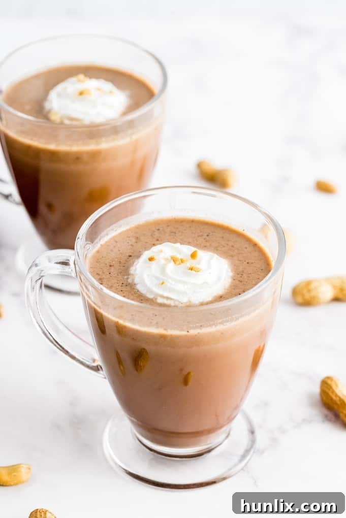Slow Cooker Peanut Butter Hot Cocoa Bliss 2 Mugs of slow cooker peanut butter hot chocolate on a white counter, topped with whipped cream and mini peanut butter cups.