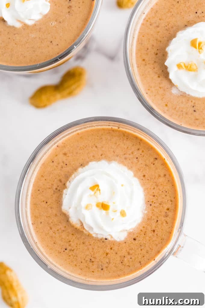 Slow Cooker Peanut Butter Hot Cocoa Bliss 3 Two mugs of slow cooker peanut butter hot chocolate on a white counter, with chocolate shavings and mini peanut butter cups.