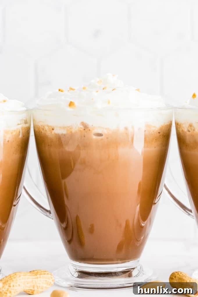 Slow Cooker Peanut Butter Hot Cocoa Bliss 4 Mugs of slow cooker peanut butter hot chocolate topped with marshmallows and chocolate drizzle.