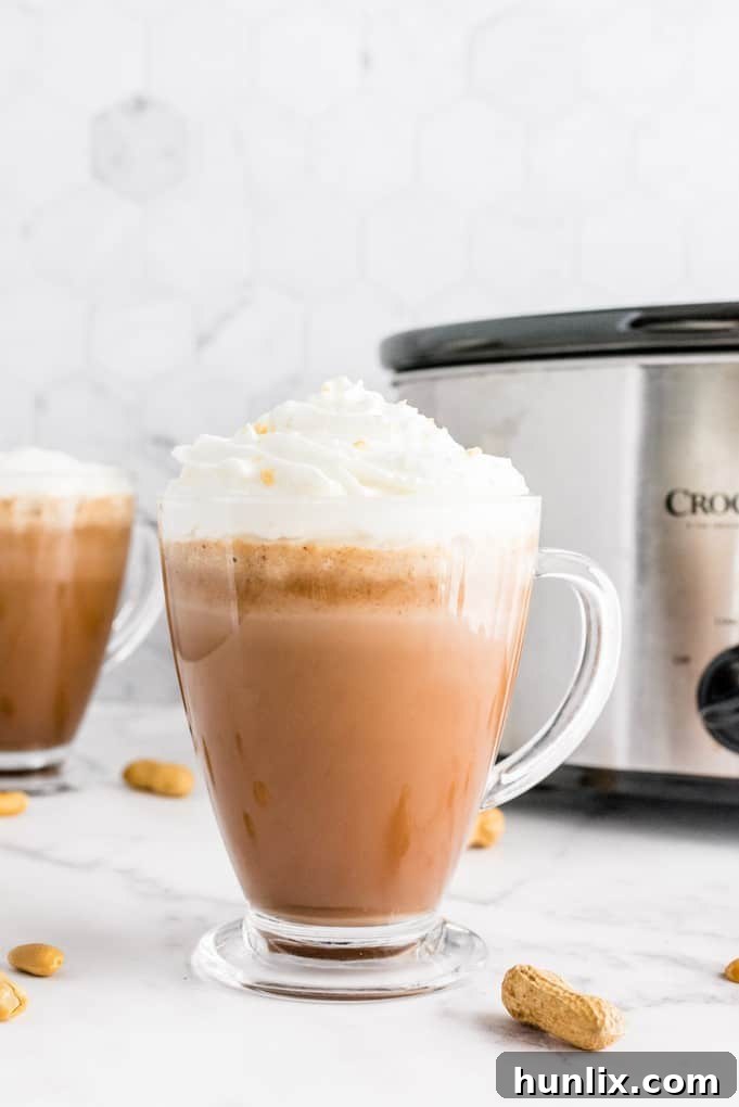 Slow Cooker Peanut Butter Hot Cocoa Bliss 6 Mugs of slow cooker peanut butter hot chocolate with a variety of toppings, including marshmallows and chocolate shavings.