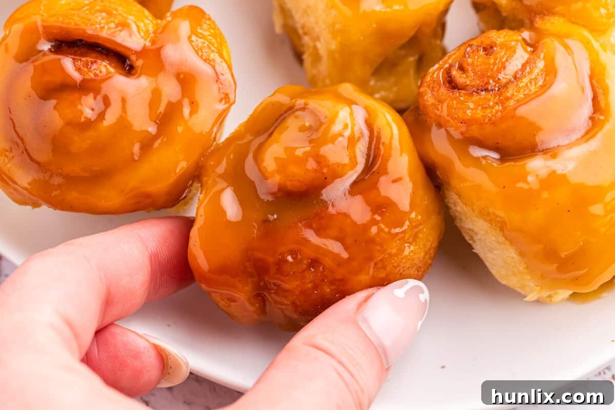 Rum-Kissed Mini Cinnamon Swirls 6 A hand holding a single Mini Rum Butter Cinnamon Roll, showcasing its sticky, saucy texture and golden brown exterior.