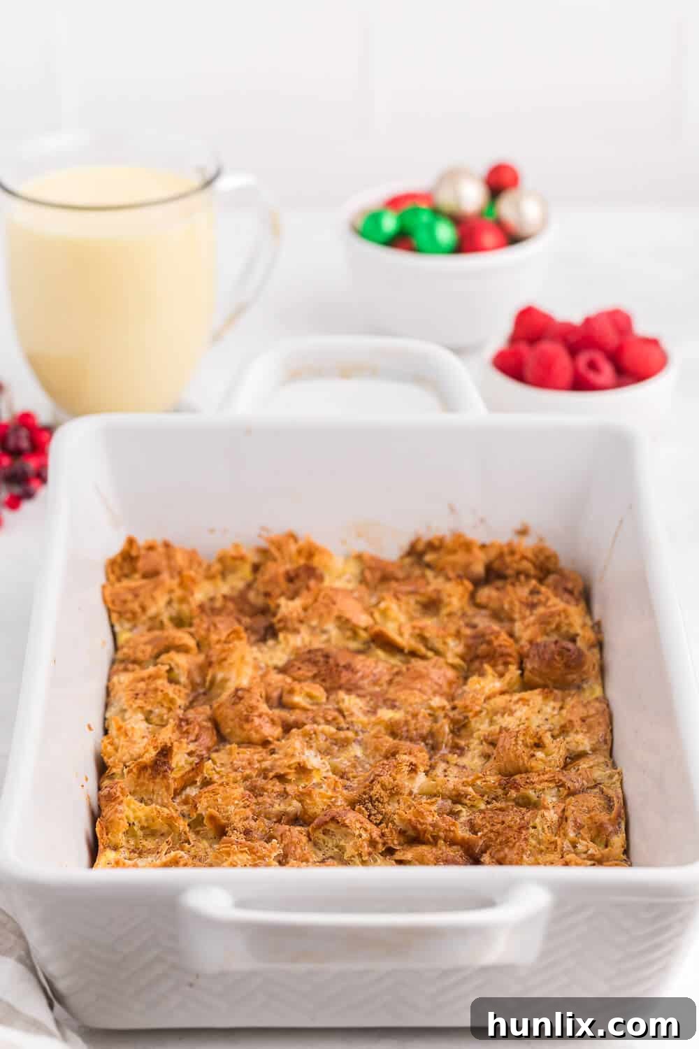 A golden brown eggnog breakfast casserole with a creamy texture, served in a white baking dish.