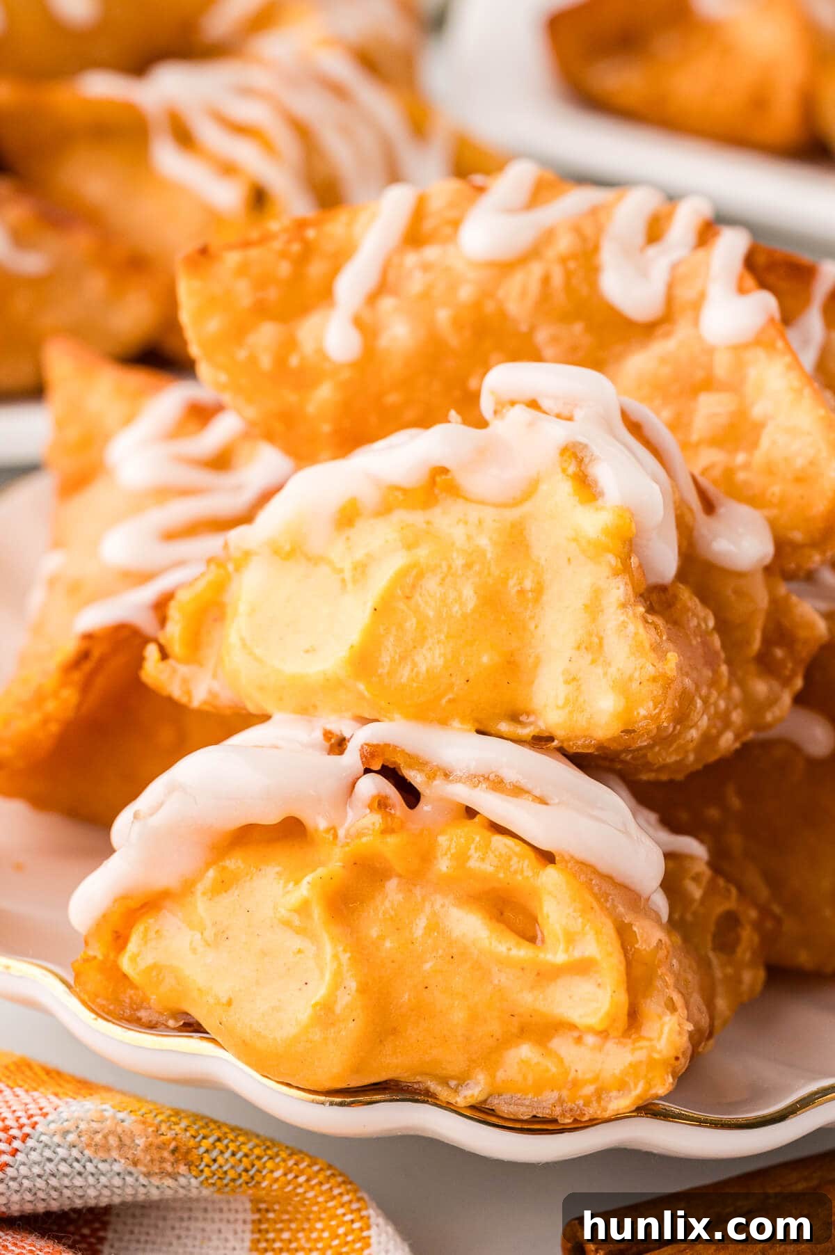 Maple-Kissed Pumpkin Cream Cheese Parcels 2 Golden-brown pumpkin cream cheese wontons arranged on a white plate, with one cut in half to reveal the creamy pumpkin filling.