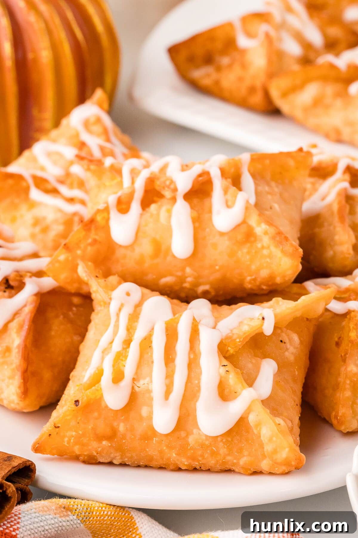 Maple-Kissed Pumpkin Cream Cheese Parcels 9 A pumpkin cream cheese wonton with maple glaze, presented on a small white plate, ready to be eaten.