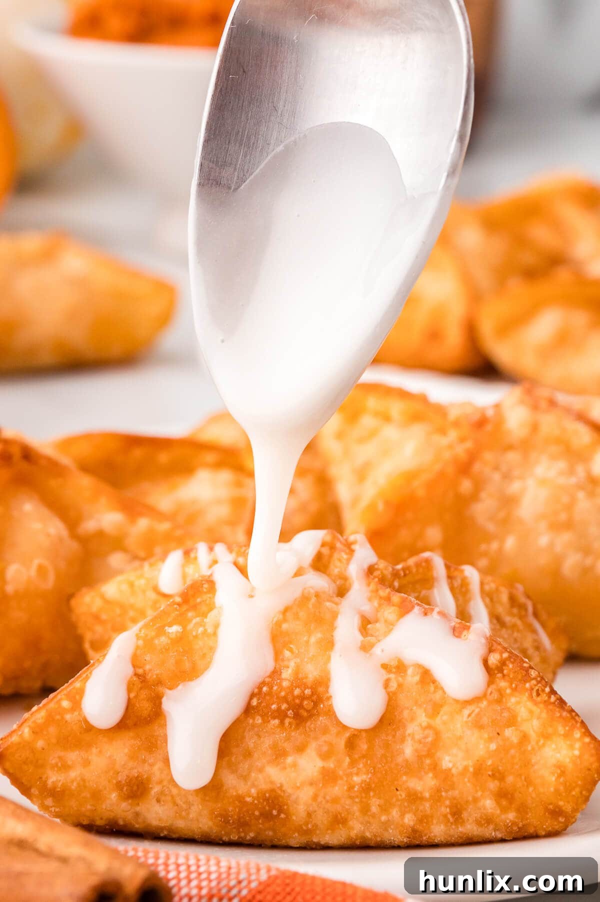 Maple-Kissed Pumpkin Cream Cheese Parcels 10 Maple glaze being drizzled over a stack of golden-brown pumpkin cream cheese wontons.