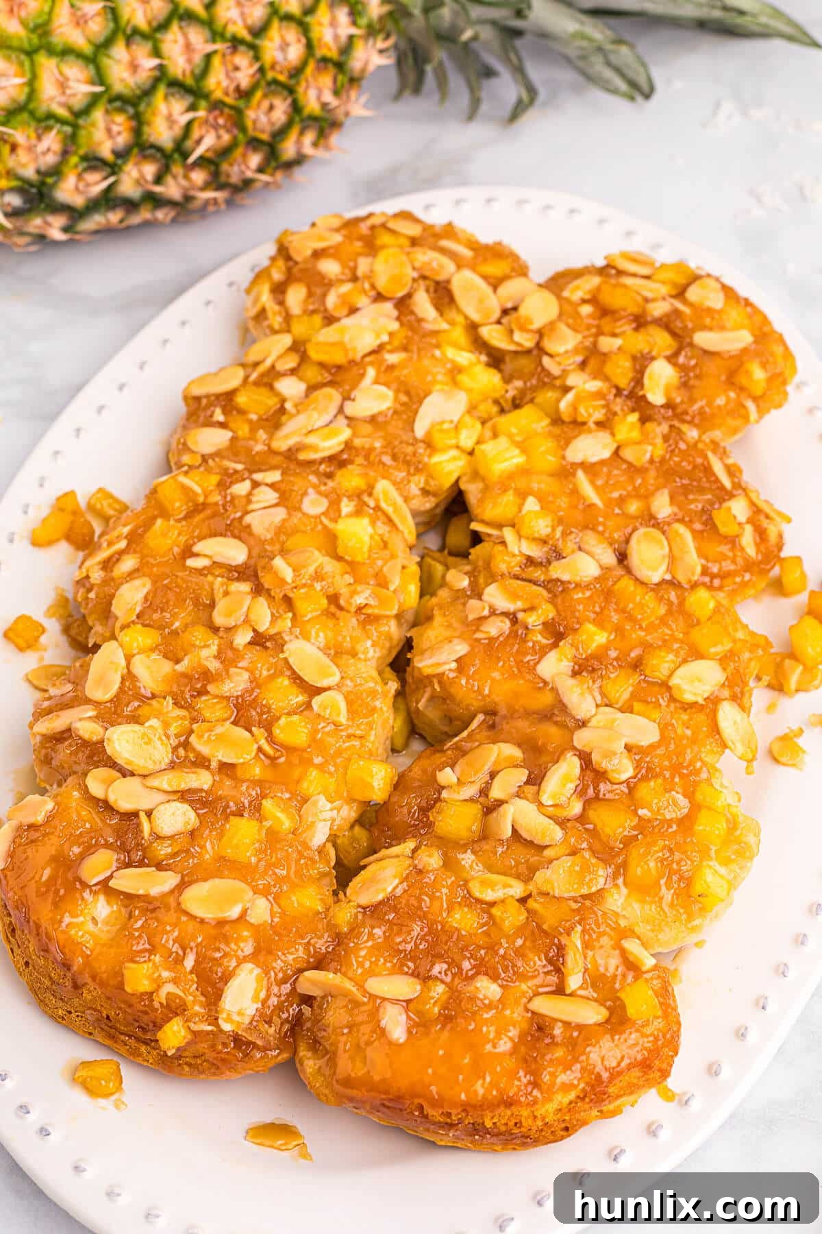 Pineapple Paradise Sticky Buns with Coconut Caramel Sauce 2 A close-up shot of golden-brown Pineapple Sticky Buns with melted coconut caramel and toasted almonds on a white platter, ready to be served.