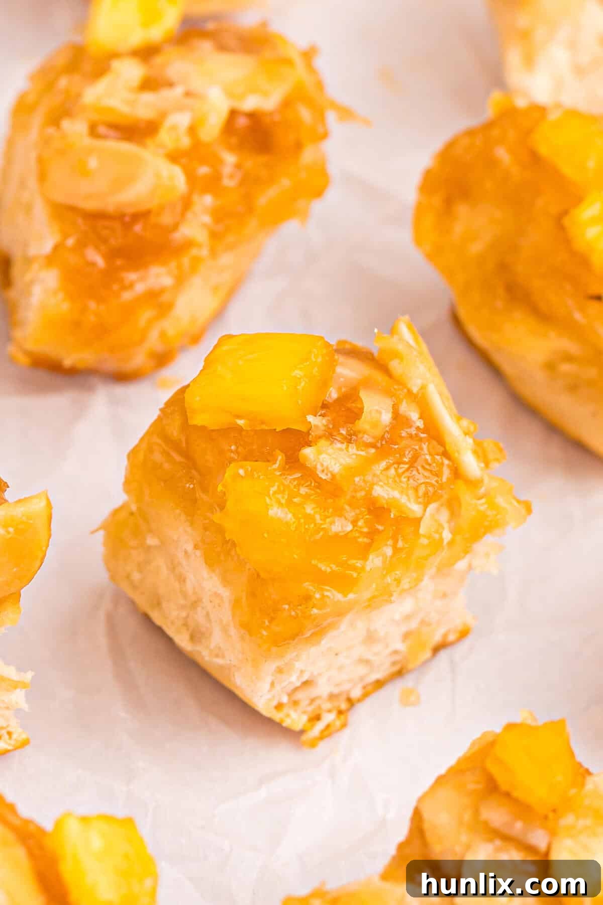 Pineapple Paradise Sticky Buns with Coconut Caramel Sauce 7 A pineapple sticky bun resting on a piece of parchment paper, showcasing its golden-brown biscuit and glossy coconut caramel topping, with visible pineapple chunks and almonds.